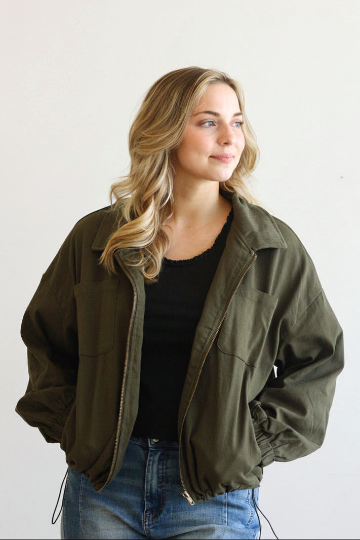 Woman wearing an olive green jacket over a black top and blue jeans on a white background