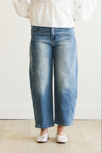 Person wearing blue jeans and a white top on a plain background
