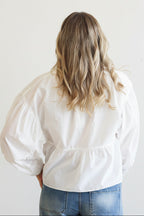 Person wearing a white blouse with puffed sleeves and blue jeans on a plain background