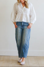 Woman wearing a white blouse and blue jeans against a plain background