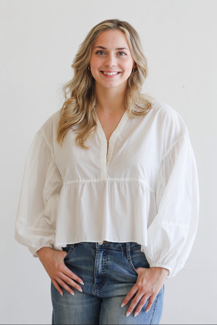 Woman wearing a white blouse and blue jeans against a plain background